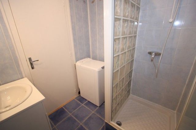 Salle d’eau avec vasque, douche et lave linge dans un coin.